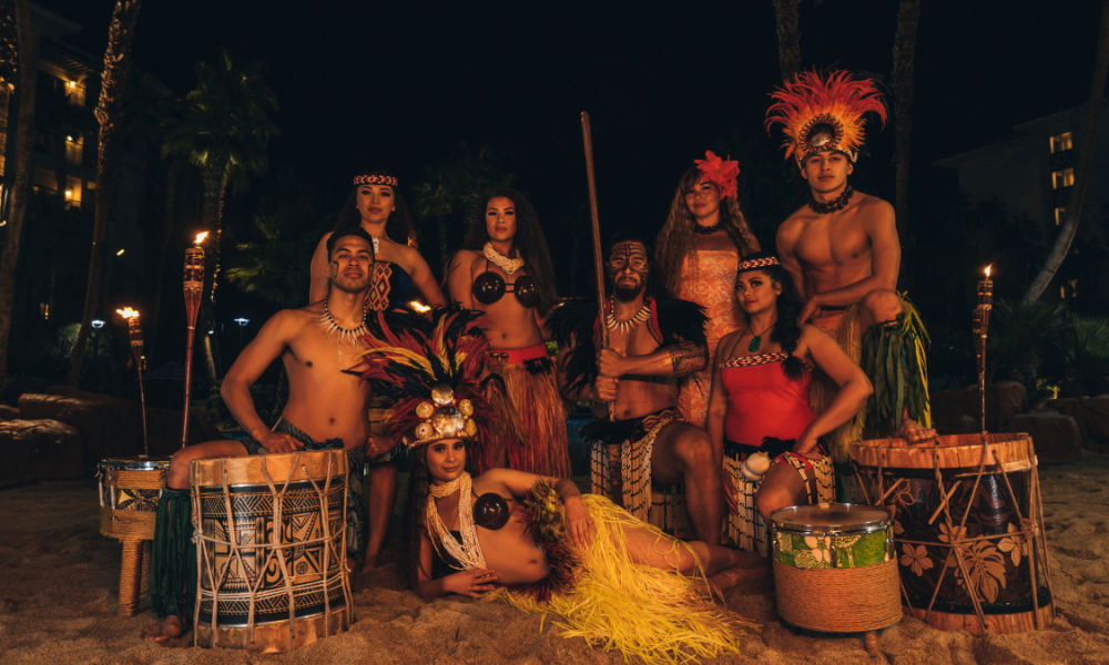Luau performers from Hot Lava Productions in full traditional Polynesian attire at Tahiti Village Resort in Las Vegas, surrounded by tiki torches and drums.