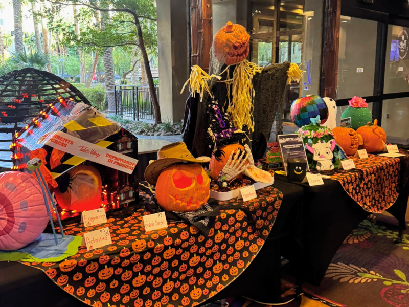 Halloween pumpkin carving display with decorated jack-o’-lanterns and scarecrow at a resort event.